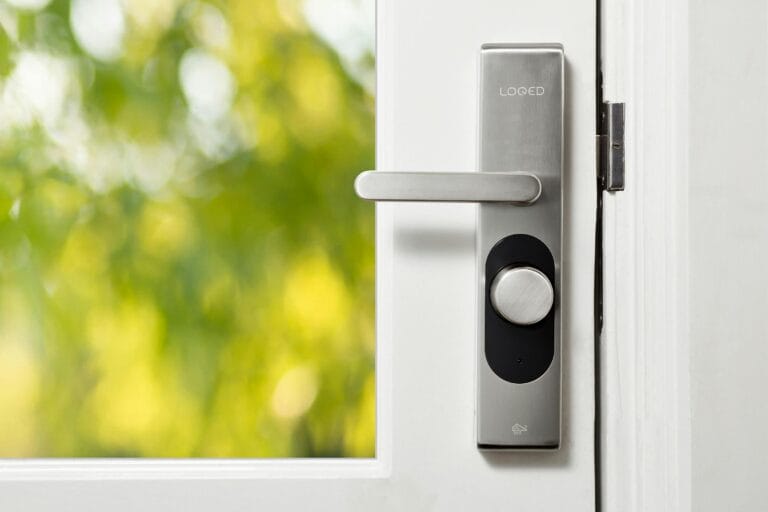 Best House Locksmith Services for Englewood Community, Sleek smart door lock on a white door with blurred green foliage in the background.